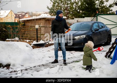 Mann schaufelt Schnee im Garten mit seinem Kleinkind. Stockfoto