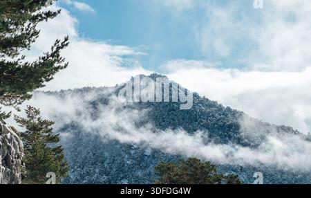 Schneebedeckter Berggipfel, umgeben von Nebel und Wolken im Winter Stockfoto