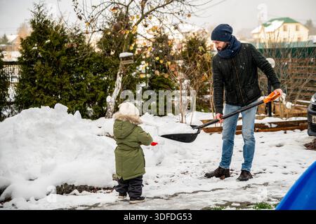 Mann schaufelt Schnee im Garten mit seinem Kleinkind. Stockfoto