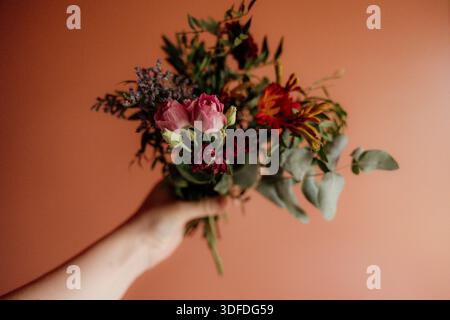 Hand hält bunten Blumenstrauß vor warmem Pastellhintergrund Stockfoto