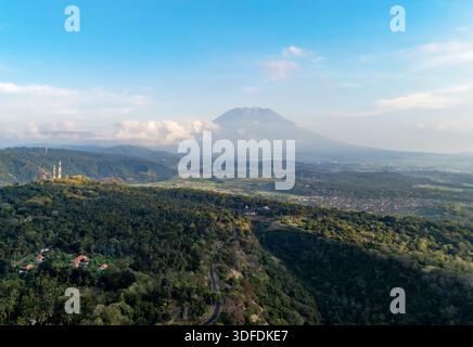 Aus der Vogelperspektive des Mount Agung umgeben von üppigen grünen Hügeln, Wäldern und Dörfern unter einem hellblauen Himmel in Bali, Indonesien. Malerische Naturlandschaft Stockfoto