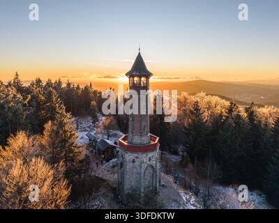 Der Stepanka-Aussichtsturm steht im Winter im Isergebirge hoch. Besucher genießen einen Blick auf den Sonnenuntergang über die Landschaft und die umliegenden Bäume in dieser ruhigen Bergkulisse. Stockfoto
