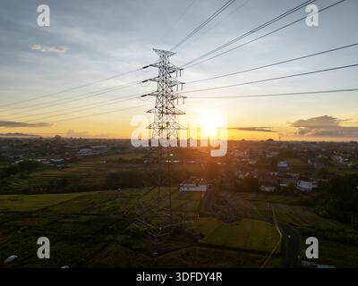 Sonnenuntergang über ländlicher Landschaft mit Hochspannungsleitungen und Sendeturm, symbolisiert Energie, Technologie und Natur in einer friedlichen Harmonie Stockfoto