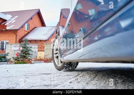 Flacher Blick auf das Autorad mit Winterreifen auf verschneite Straße in der Nähe eines Wohnhauses. Konzept für Winterfahren, Straßensicherheit, kalte Witterungsbedingungen und Stockfoto
