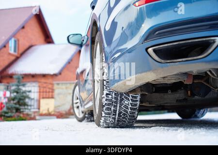 Flacher Blick auf das Autorad mit Winterreifen auf verschneite Straße in der Nähe eines Wohnhauses. Konzept für Winterfahren, Straßensicherheit, kalte Witterungsbedingungen und Stockfoto