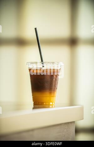 Eiskaffee-Getränk mit schwarzem Kaffee, das über Orangensaft gelegt und in einer klaren Tasse zum Mitnehmen über Eis serviert wird. Stockfoto