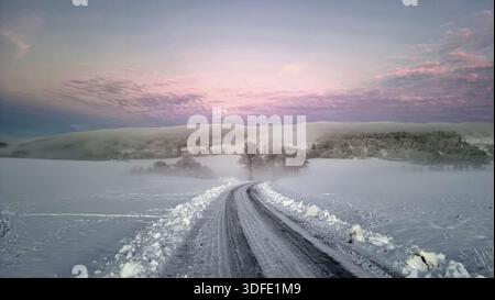 Ein schneebedeckter Weg führt durch eine winterliche Landschaft unter einem pastellfarbenen Sonnenuntergang mit rosa Wolken. Dämmerung, der Mond scheint durch den Nebel. Vollmondaufgang atmosp Stockfoto