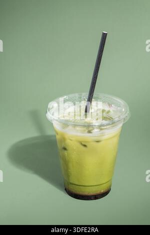 Gefrorener Matcha Latte serviert über Eis in einer klaren Tasse zum Mitnehmen. Cremiges grünes Teegetränk, fotografiert auf einem sauberen, minimalen Studiohintergrund. Stockfoto