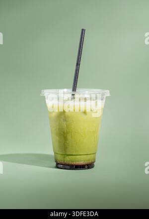 Gefrorener Matcha Latte serviert über Eis in einer klaren Tasse zum Mitnehmen. Cremiges grünes Teegetränk, fotografiert auf einem sauberen, minimalen Studiohintergrund. Stockfoto