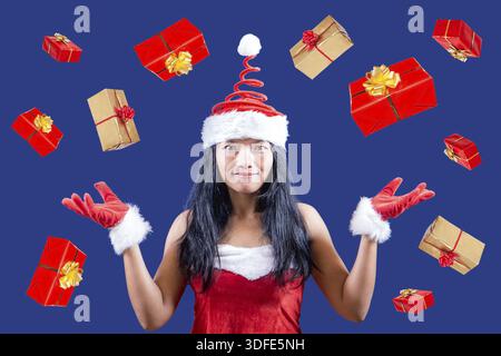 Die fröhliche Mrs. Claus schaut in die Kamera und jongliert mit Weihnachtsgeschenken. Weihnachtsboxen fallen um Mrs. Santa Claus herum. Mrs. Claus gibt Geschenke Stockfoto