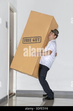 Der Postbote trägt ein großes Paket - kostenloses Geschenk. Der Postdienst bringt eine große Ladung in die Wohnung Stockfoto