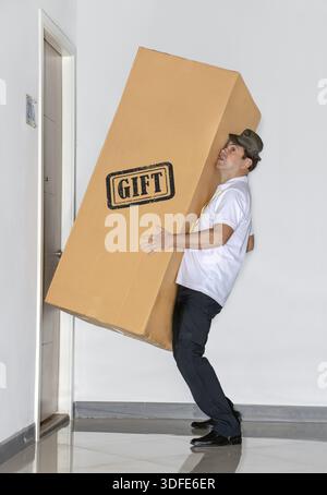 Der Postbote trägt ein großes Paket - ein Geschenk. Der Postdienst bringt eine große Ladung in die Wohnung Stockfoto
