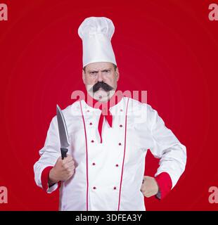 Strikter Koch, der ein Messer auf rotem Hintergrund hält Stockfoto