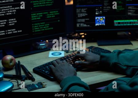 Junger schwarzer Mann, der Code auf der Computertastatur im dunklen Büro eingibt Stockfoto