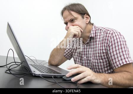Der verwirrte, unglückliche Benutzer schaut auf den Computerbildschirm. Ein überraschter, gestresster Mann, der auf einen Laptop Systemfehler auf dem Computer Stockfoto