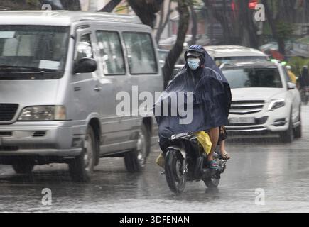 Leute mit Regenmantel fahren im Regen auf einem Motorrad. Transport in der Stadt, wenn es regnet Stockfoto