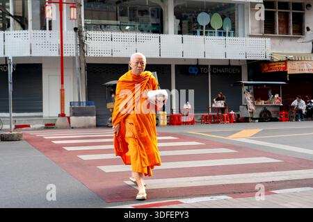 Hatyai, Thailand - 26. August 2024: Buddhistische Mönche in orangen Gewändern empfangen Morgenalmosen von einer knienden Frau auf einer Straße in Thailand. Stockfoto