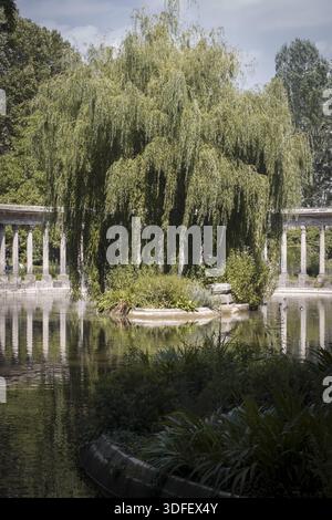 Der Blick auf die Trauerweide zieht die grünen Zweige über einen ruhigen Teich, der von einer klassischen Kolonnade eingerahmt wird, und schafft eine ruhige Oase in Paris, Îl Stockfoto