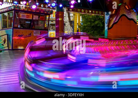 Eine schnelle Fahrt beim Sommerfest im Olympiapark München. Expresszug in Bewegung, Unschärfe und Ticketschalter mit farbenfroher Disco-Beleuchtung Stockfoto