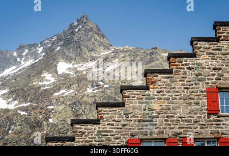 Steingebäude mit roten Fensterläden vor Bergkulisse. Stockfoto