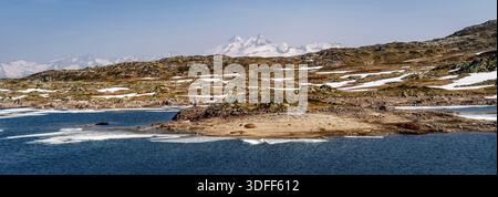 Eine ruhige Landschaft mit einer felsigen Küste, Schneeflocken und fernen Bergen unter einem klaren Himmel. Stockfoto