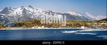 Schneebedeckte Berge und ein teilweise gefrorener See unter einem klaren blauen Himmel. Stockfoto