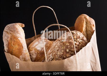 Papiertüte mit Brotsortiment auf schwarzem Hintergrund Stockfoto