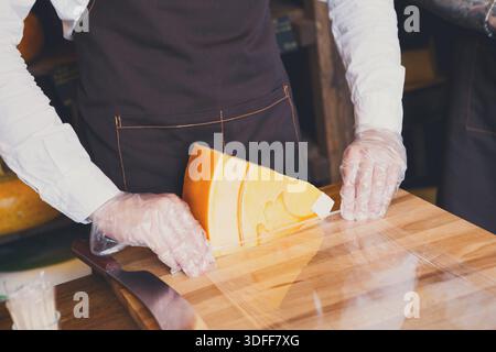 Der Ladenassistent wickelt ein Stück Käse ein Stockfoto