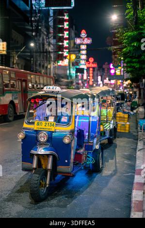Bangkok, Thailand - 11.11.2025: Tuk Tuk wartet nachts auf der Yaowarat Road in Bangkok Chinatown, mit leuchtenden Neonschildern dahinter und Touristen zu Fuß Stockfoto