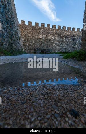Leiria. Ein Niedrigwinkelfoto fängt die alten Steinmauern einer Burg mit ihren zinnenbesetzten Zinnen ein, die sich perfekt in einer Pfütze auf dem Kies spiegeln Stockfoto
