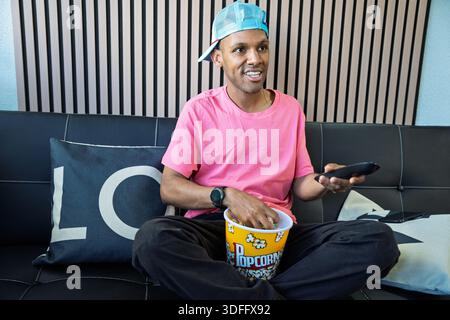 Junger Mann, der Freizeit auf dem Sofa genießt, Fernsehen schaut und Popcorn isst Stockfoto