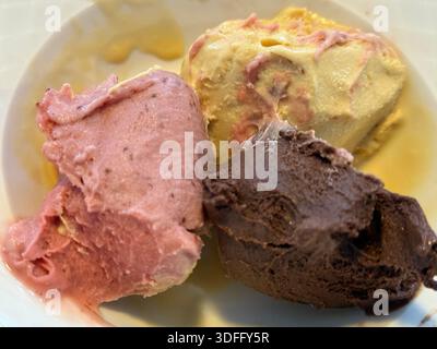 Schaufeln mit Erdbeeren, Vanille und Schokoladeneis in einer Schüssel-Nahaufnahme. Mobiles Foto Stockfoto