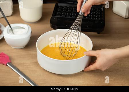 Mit einem Schneebesen die rohen Eier in einer weißen Schüssel zum Backen von Waffeln mischen. Stockfoto