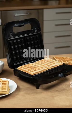 Frisch gebackene goldene Waffeln in einer offenen elektrischen Waffelmaschine Stockfoto
