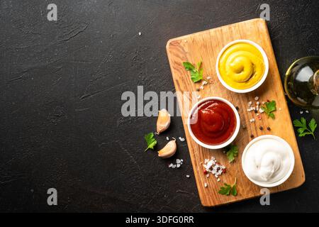 Ketchup, Mayonnaise und Senf in den Schalen auf dem Schneidebrett. Draufsicht, Platz für Konstruktion. Stockfoto
