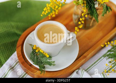 Frisch gebrühter Kaffee mit Mimosa-Blüten auf einem Holztablett Stockfoto