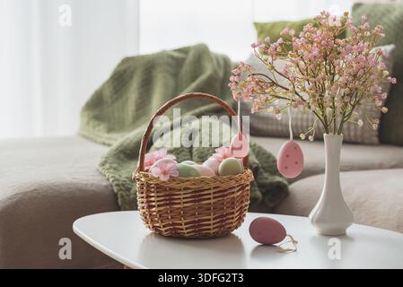 Osterkorb mit Ester-Eiern, Plüschhase und Frühlingsdekor auf weißem Tisch im Cozy Wohnzimmer Stockfoto
