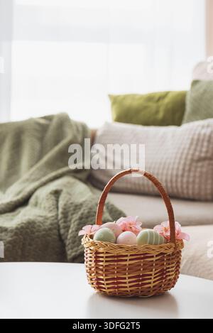 Osterkorb mit Ester-Eiern, Plüschhase und Frühlingsdekor auf weißem Tisch im Cozy Wohnzimmer Stockfoto