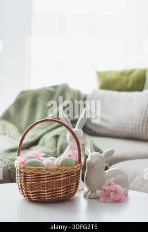 Osterkorb mit Ester-Eiern, Plüschhase und Frühlingsdekor auf weißem Tisch im Cozy Wohnzimmer Stockfoto