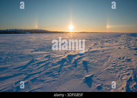 SunDog oder Parhelion mit Paaren von Scheinsonnen bei 22 Grad auf jeder Seite der Sonne, bei Sonnenaufgang über dem gefrorenen See in Yellowknife Bay, NT, Kanada. Stockfoto