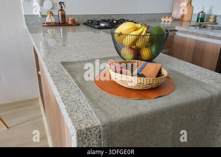 Granitinsel-Arbeitsplatte mit Obst in einem Drahtkorb und einer kleinen gewebten Schüssel Stockfoto