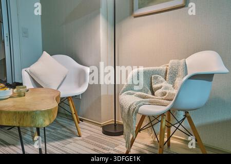 Minimalistische Inneneinrichtung mit Stühlen im Stil der Mitte des Jahrhunderts, einem Holztisch und warmer Beleuchtung Stockfoto