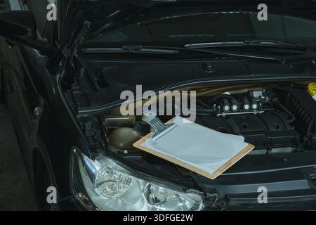 Fahrzeugmotor mit Klemmbrett und leerem Papier als Symbol für Fahrzeuginspektion und -Wartung Stockfoto