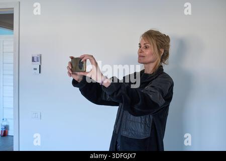 Frau mittleren Alters, die während der Immobilienbesichtigung Smartphone-Fotos von der Wohnung macht Stockfoto