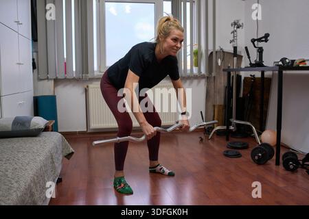 Frau mittleren Alters, die sich während des Heimtrainings über Langhantelreihen gebeugt hat Stockfoto