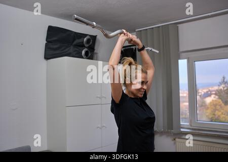 Frau mittleren Alters, die während des Heimtrainings eine Trizepsverlängerung mit Langhantel macht Stockfoto
