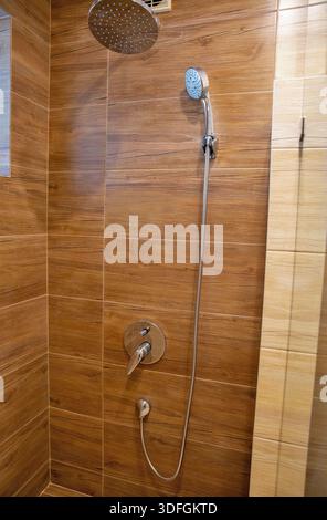 Modernes Badezimmer mit Dusche mit Holzmaserung, Porzellanfliesen, Chrom-Regenduschkopf, Handspray und Hebelbedienelementen. Sauber Stockfoto
