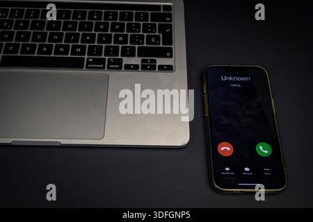 Nahaufnahme eines Laptops und Smartphones mit einem eingehenden Anruf von einer unbekannten Nummer. Konzept von Spam, Datenschutz, Unterbrechungen und digitaler Sicherheit. Stockfoto