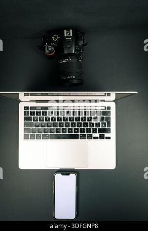 Flache, von oben nach unten liegende Laptoptastatur mit DSLR-Kamera und leerem Smartphone-Bildschirm auf dunklem Hintergrund. Minimaler technischer Arbeitsbereich mit Kopierraum. Stockfoto