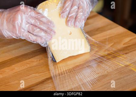 Der Ladenassistent wickelt ein Stück Käse ein Stockfoto
